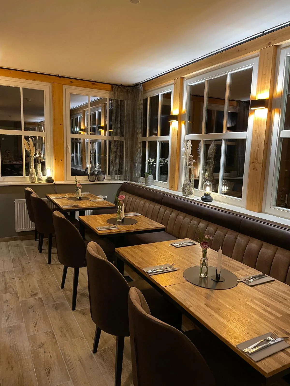 Wintergarten mit großen Fenstern, Holztischen und gepolsterter Sitzbank am Abend