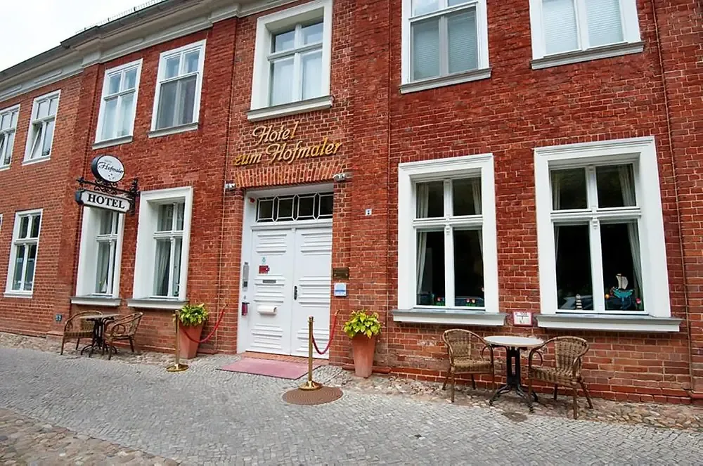 Rote Backsteinfassade des Hotels zum Hofmaler mit Eingang und Sitzplätzen